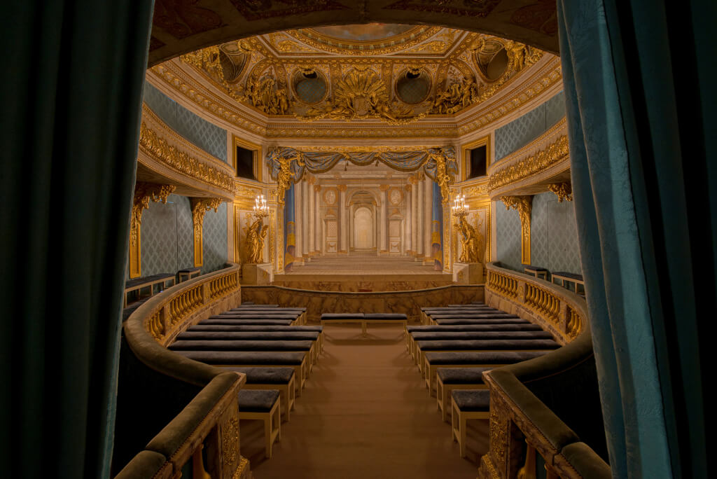 Intérieur du Petit Théâtre de la Reine : vue sur la salle avec lumière ambiante ; en fond, décor de scène du Temple de Minerve, par les frères Slodtz (1754). © Château de Versailles / Thomas Garnier.